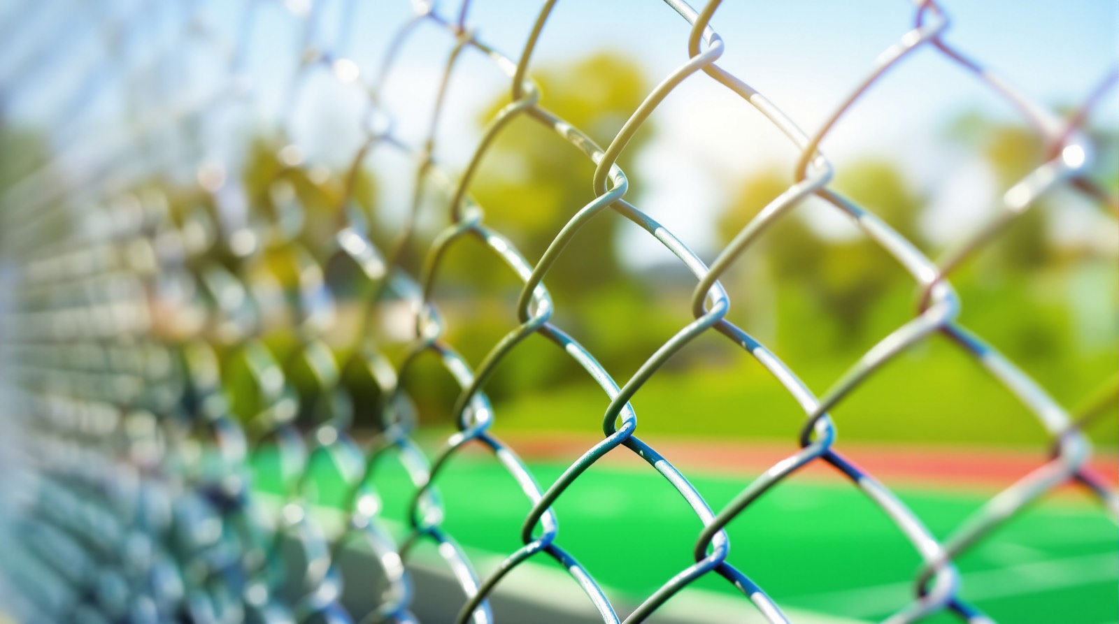 Galvanized chain link fence with diamond mesh pattern along a sports field